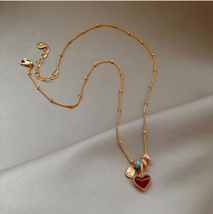 Detail of 18k gold plated chain with red heart pendant and engraved charm on silk