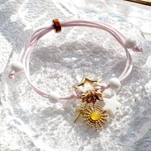 Close-up of pink woven DIY bracelet with golden sun and star charms on glass