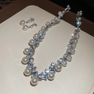 Macro shot of French vintage diamond rhombus pearl necklace and earrings set on beige display