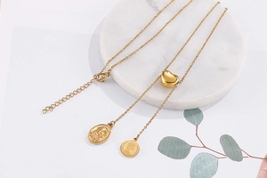 Detail of layered gold necklaces with heart and coin pendants on marble background