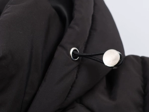 Close-up of black puffer jacket hem featuring adjustable elastic drawstring and silver metal toggle