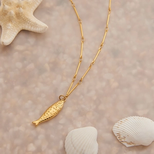 Detail der 18K Gold Fisch Halskette am Strand mit Seesternen und Muscheln