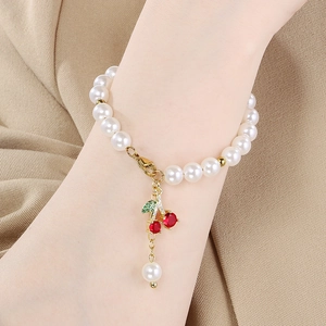 Close-up of pearl bead bracelet featuring a sparkling cherry pendant with red crystals