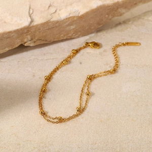 Detail of elegant 18K gold-plated double-layer bead chain bracelet on a stone surface
