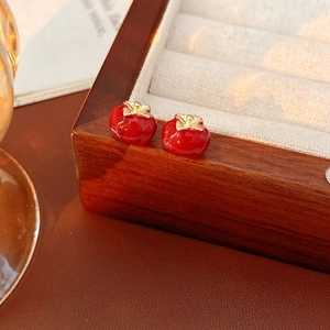 Close-up of red persimmon earrings with gold leaf detail on a vintage jewelry box