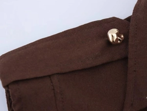 Dettaglio del tessuto in lino e bottone dorato su abito a camicia senza maniche marrone