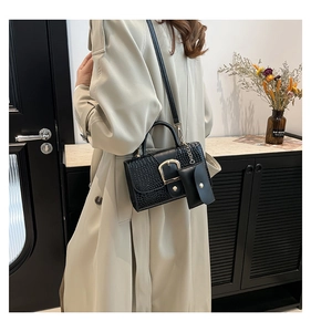 Détail du sac à main noir motif crocodile avec boucle dorée et mini pochette décorative