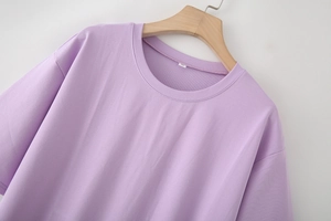Detailaufnahme von hellviolettem Strickkleid-Ausschnitt mit S-Etikett am Holzbügel