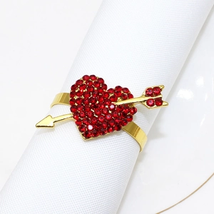 Macro detail of golden heart napkin ring with red rhinestones and arrow on white linen