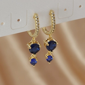 Detail of gold earrings with blue round zircons on champagne silk background