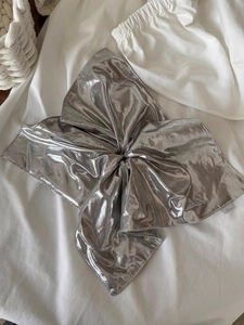 Detail of silver metallic fabric scrunchie with twisted knot and brand tag on white fabric