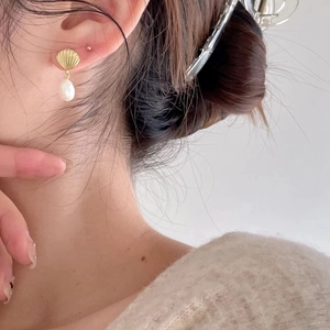 Close-up of gold shell stud earrings with white freshwater pearl pendants on a model