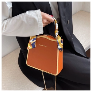 Detail of a brown orange box bag featuring a silk scarf handle and golden chain strap