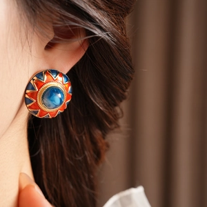 Detail of vintage round enamel earring with blue gemstone and gold edge on ear