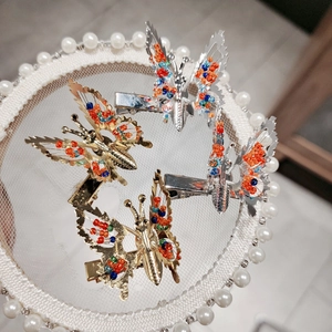 Detailed view of beaded butterfly hair clips in gold and silver on a lace tray