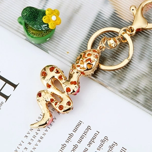 Detail of golden snake keychain with red rhinestones, clasp, and bell on a magazine