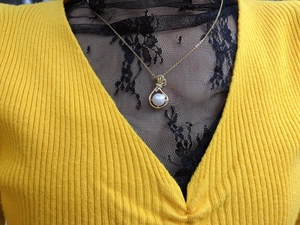 Detail of elegant gold teardrop necklace with freshwater pearl and zircon on yellow sweater