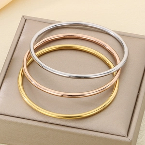 Close-up of three minimalist polished bangles in gold, rose gold, and silver finishes