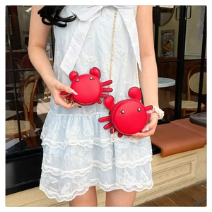 Detail view of red crab-shaped mini crossbody bag with gold chain strap on a blue dress