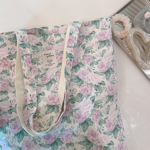 Close-up of floral cotton tote bag with pink rose patterns and woven handles on a desk