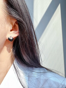 Dettaglio di orecchini a lobo neri a forma di cuore in argento indossati da modella