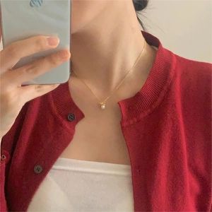 Close-up of a delicate bow and pearl pendant necklace worn with a red sweater