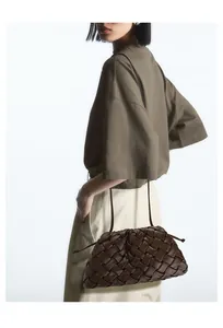 Detail of dark brown woven leather crossbody bag with pleated texture on model
