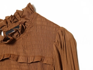 Detail of smocked chest design and ruffled neckline on brown ruched woven top