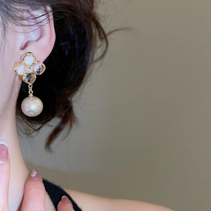 Detail view of gold-plated four-petal flower earrings with large pearls worn by model