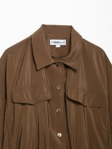 Détail d'une chemise safari marron avec col à revers, boutons métalliques et poches poitrine