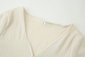 Detail of V-neck opening and textured seersucker fabric on beige long-sleeve top