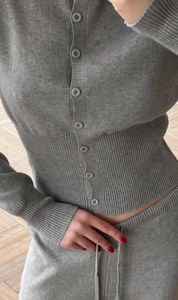 Detail of grey knitted cardigan with buttons and matching drawstring trousers on wood floor