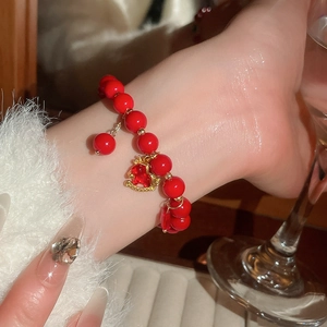 Close-up of red beaded bracelet with golden crown and heart pendant on wrist