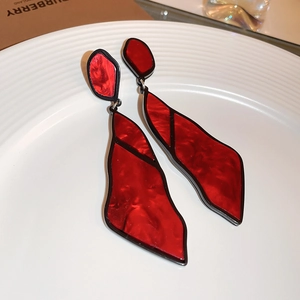 Macro detail of geometric red and black acrylic drop earrings with marble texture on white plate