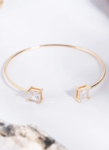 Macro detail of gold-plated open bangle featuring two square-cut clear crystals