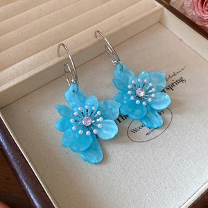 Detail of light blue resin flower earrings with pearl centers and silver hooks in a box