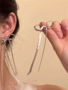 Detailed close-up of silver bow earrings with long hanging chain tassels on model