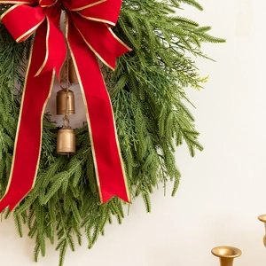Close-up of Christmas wreath with red ribbon bow and vintage brass bells on pine needles