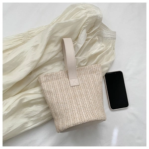 Top view of straw bucket bag with herringbone weave on a white dress with phone for scale