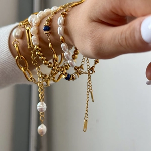 Detail of layered 18k gold stainless steel bracelet with pearls and blue beads on wrist