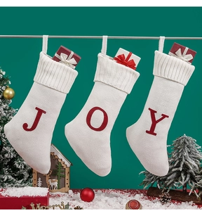 Detailed close-up of three white knitted Christmas stockings with red J O Y embroidered letters