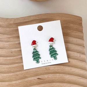 Detail of Christmas tree earrings with red Santa hat charms on a wooden display tray