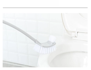 Detail of curved long-handle toilet brush cleaning under the rim of a white ceramic commode