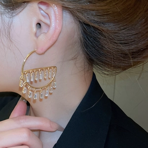 Close-up of golden geometric earrings with rectangular zircons on model ear