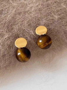 Macro shot of 18k gold plated tiger eye stone earrings on soft plush background