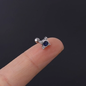 Macro shot of silver stainless steel cartilage stud with blue zircon held on a fingertip