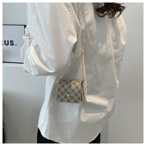 Close-up of mini crossbody chain bag with beige monogram pattern on a white shirt