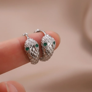 Macro shot of a silver snake hoop earring with green gemstone eyes on a fingertip