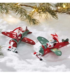 Detail of metal Christmas airplane ornaments with Santa and snowman on snowy pine branches