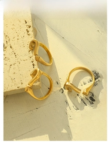 Three gold question mark rings displayed on a beige stone slab with soft natural lighting